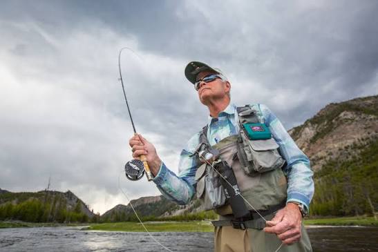 An angler casting a fly line into a misty, scenic river at dawn